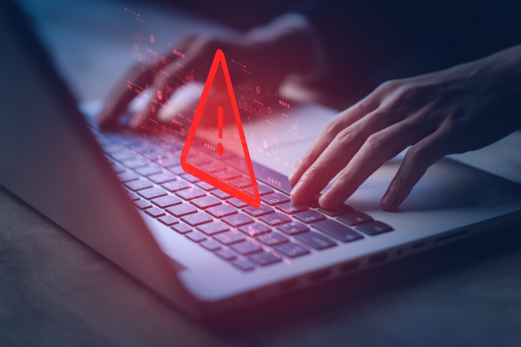 A person typing on a laptop that has a danger caution triangle on it.