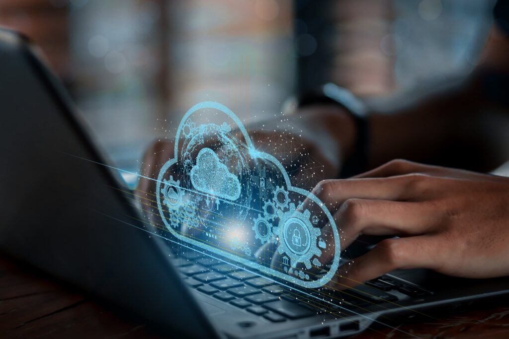 an individual interacting with their laptop with a hologram above the keyboard displaying a cloud with working security parts.